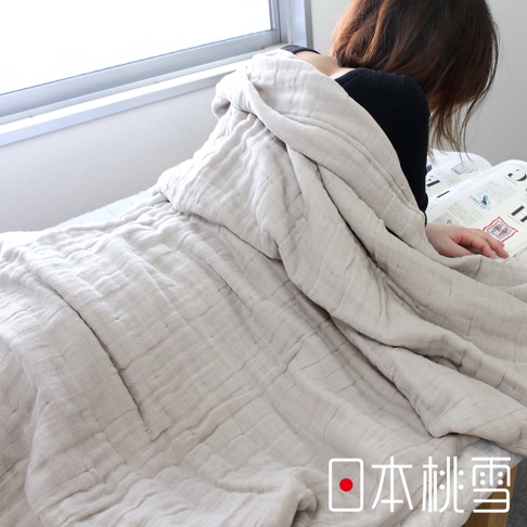 一層淺米色八層紗透氣被，質感柔軟，表面有自然的皺褶紋理，覆蓋在一名正在閱讀的女子身上，背景為窗戶和床鋪。