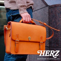 職人手作皮革經典三扣兩用商務公事包，以橙色皮革製成，設有金色扣環和可調節肩帶，適合商務場合使用。