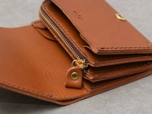 一個棕色皮革雙折迷你短夾，展示了拉鍊開合、金屬壓扣和手縫細節。