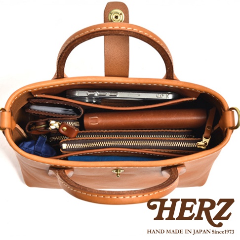 職人手作皮革迷你托特包 T-11，展示包內物品：手機、長夾、錢包、鑰匙包、藍色收納袋。包身為棕褐色皮革，縫線明顯，質感佳。