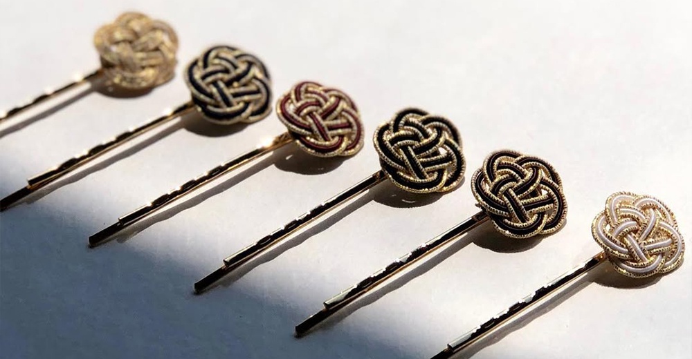 一排六個髮夾，頂端有以金絲編織的日式水引花結，顏色包含金色、黑金、紅金、黑白。髮夾為細長的金色金屬材質。
