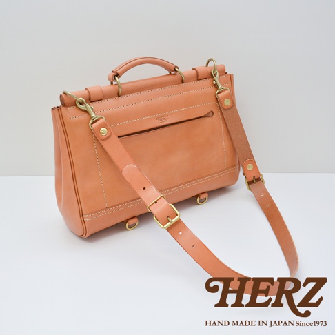 日本HERZ職人手作皮革瓦風側背包，淺棕色皮革，附有可拆卸斜背帶，上面壓印有HERZ品牌字樣及HAND MADE IN JAPAN Since1973字樣。