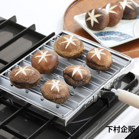 不鏽鋼材質的瓦斯爐專用燒烤盤，烤架上擺放著六顆烤至金黃的香菇，香菇頂部有十字切紋，一側配有木質手柄。