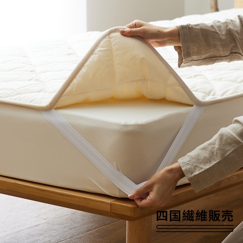 雙人加大床墊，奶油色，表面有菱格紋縫線，邊緣為米色滾邊。床墊有四個鬆緊帶固定在床墊上。