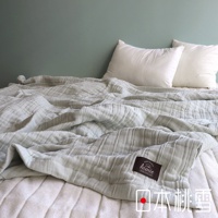 淺灰色八層紗雙人透氣被，材質為純棉，呈現褶皺紋理，帶有深棕色品牌標籤，放置於雙人床上，背景為淺綠色牆面，搭配兩個白色枕頭。