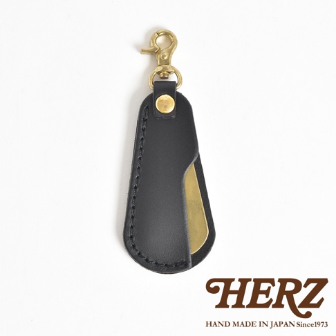 黑色皮革包覆金色金屬鞋拔，附有黃銅釦環及吊飾，整體設計簡潔實用。