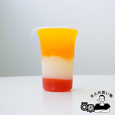 杯子裡裝著三種顏色分明的果凍，由下至上分別為紅色、白色和黃色，頂部蓋著透明塑膠膜。