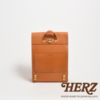 棕色皮革製作的紙袋風後背包，正面有貼袋和品牌標誌，頂部有提把和金屬扣環，底部有兩個金屬環。