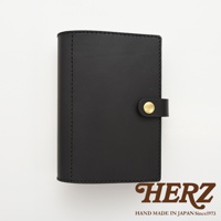 黑色皮革手帳/記事本書套，帶有金色釦件，左側邊緣有縫線細節。