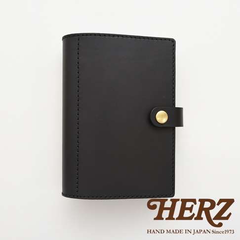 黑色皮革手帳/記事本書套，帶有金色釦件，左側邊緣有縫線細節。