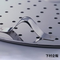 銀色金屬製的平底鍋專用萬用蒸盤，盤面佈滿圓形孔洞，中央設有彎曲狀的金屬提把，提把透過铆釘固定在蒸盤上，整體呈現光澤。