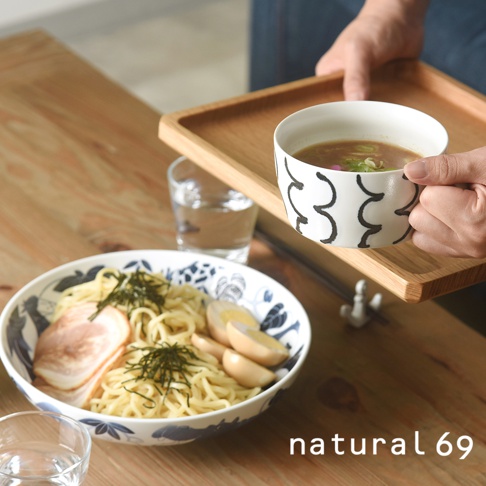 手繪附耳湯杯，白色陶瓷杯身繪有黑色線條紋飾，盛有熱湯與蔥花，由手持於木質托盤上，旁邊另有裝有麵食的藍白花紋大碗。