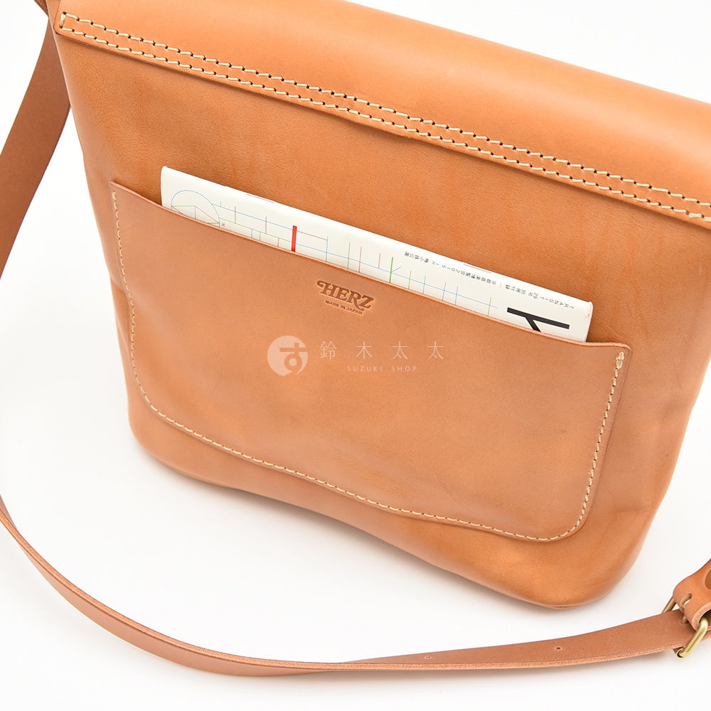 一個棕色皮革郵差包，正面有一個開口小袋，裡面露出了一本筆記本。