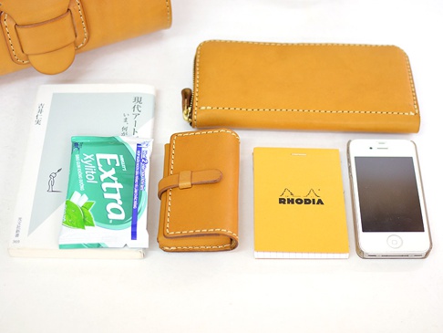 數件原色皮革小物，包含長夾、鑰匙包、手機、筆記本及口香糖，皆以白色背景呈現。