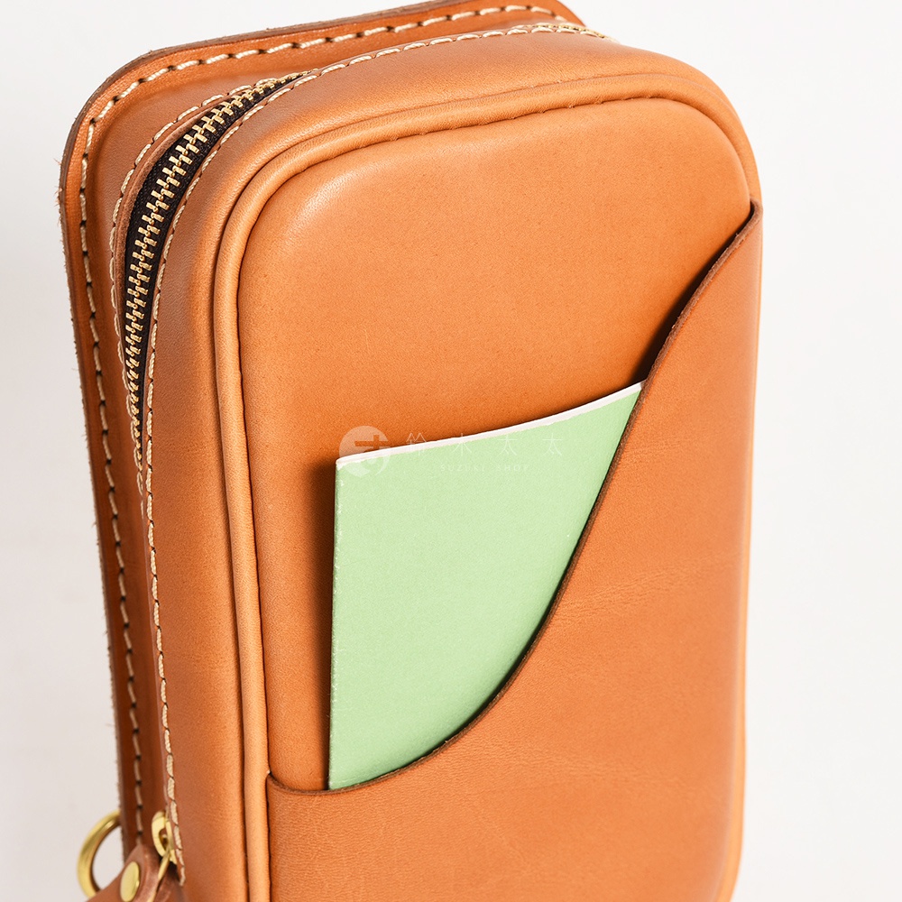 HERZ 品牌手工皮革直立型斜背包，展示細節，咖啡色皮革拉鍊及側面口袋，口袋中可見一張綠色紙。