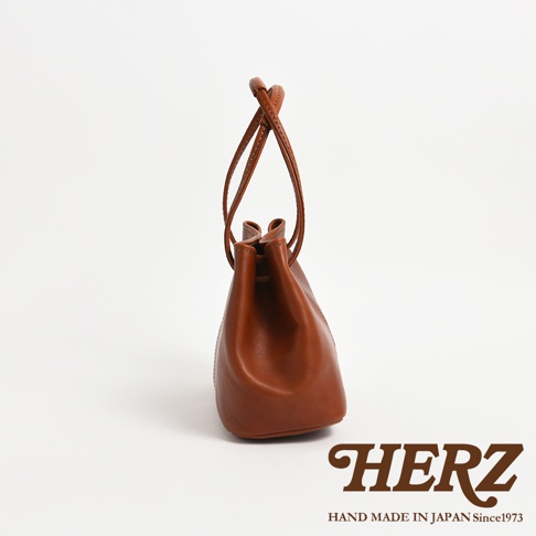 HERZ 品牌標誌及 HAND MADE IN JAPAN Since1973 字樣，搭配一褐棕色皮革製成的束口袋。