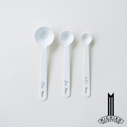 三支不同容量的白色琺瑯計量匙，分別標示 15cc、5cc 和 2.5cc，一旁還有品牌 logo。