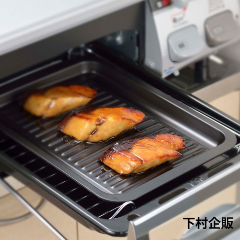 黑色金屬多功能萬用波浪烤盤，盤內有三塊烤製金黃、表面帶有醬汁的魚塊，烤盤置於烤箱內。