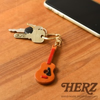 職人手作皮革吉他造型鑰匙圈，主體為橘棕色皮革，吉他面板飾有黑色與紅色皮革點綴。