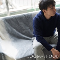 一款淺灰色漸層短絨單人毯，觸感柔軟，覆蓋在沙發上，一名穿著海軍藍連帽衫和灰色運動褲的男子坐在毯子上。