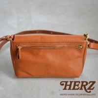 一個棕褐色的皮革斜背包，正面有一個拉鍊口袋，並附有皮革背帶。