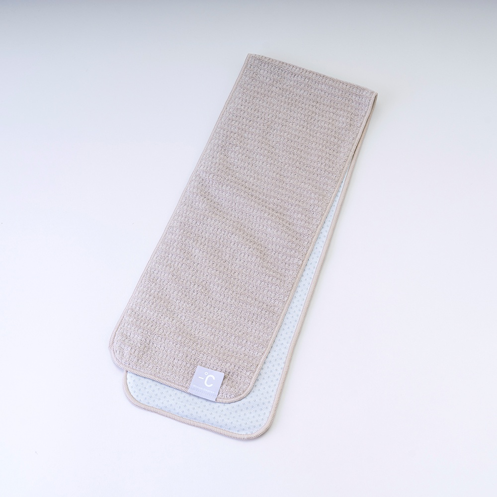 一條淺棕色、紋理細緻的降溫涼感毛巾，另一面為淺藍色，帶有細小網格紋路。毛巾一角縫有標有 -C 字樣的白色小標籤。