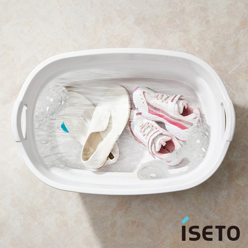 白色伸縮浴盆內有水，盆中放著一雙白色平底鞋和一雙粉白色運動鞋，有部分氣泡。