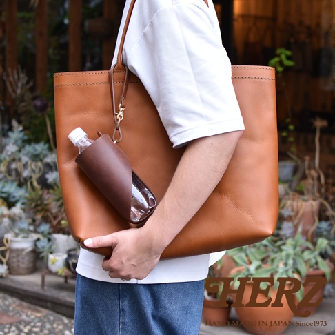 職人手作皮革Organ水壺套，深棕色皮革，附有金屬扣環，可掛於同色系皮革托特包上，包內裝有透明水瓶。