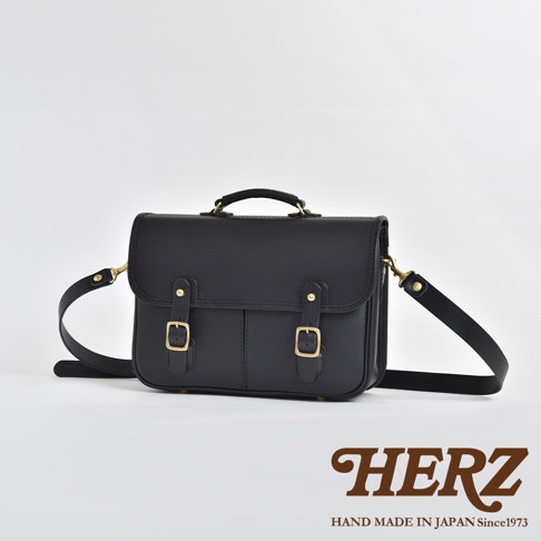 黑色皮革製成的手提/單肩兩用包，帶有兩個前袋、金色搭扣和可調節肩帶。