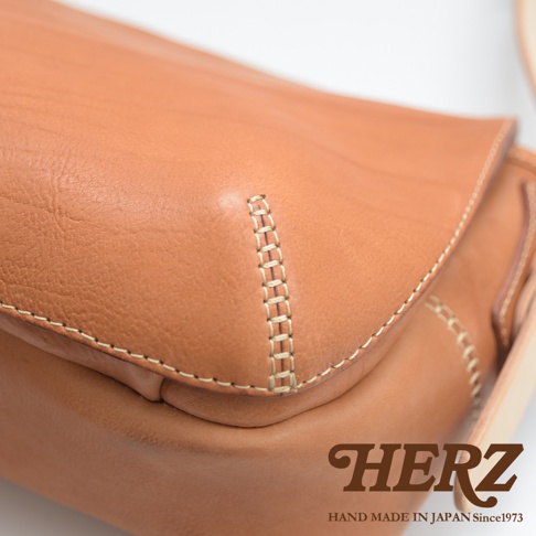 淺棕色皮革郵差包特寫，展示手工縫線細節，包體呈現自然的皮革紋理。