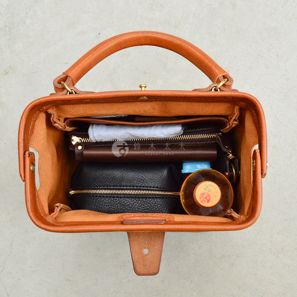 職人手作皮革Organ方形口金托特包，棕色皮革，內部裝有咖啡色長夾、黑色化妝包、白色紙巾和一瓶飲料。