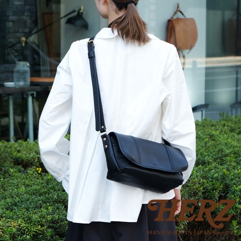 黑色皮革復古郵差包，包身有縫線裝飾，可調節長度的黑色皮革肩帶，使用黃銅五金配件。