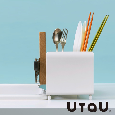 白色方形瀝水架，內含不鏽鋼湯匙、叉子、兩雙筷子（一雙橘色、一雙綠色）及白色盤子，架旁掛著木質砧板。