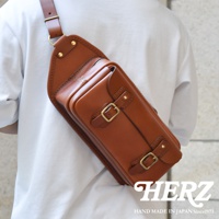 職人手作皮革騎士隨身斜背包，採用棕色皮革製成，設有拉鍊主袋和兩個帶有黃銅扣的翻蓋前袋，肩帶可調節。