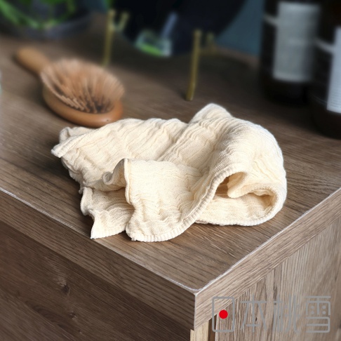 日本桃雪立體褶皺柔綿紗布洗臉巾，以淺黃色皺褶紗布材質製成，放在木紋櫃子上，背景有木柄梳子和瓶子。