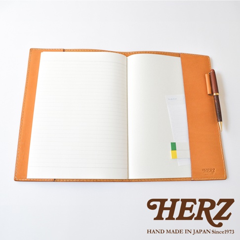 攤開的日本HERZ職人手作淺棕色皮革筆記本書套，內部右側設有專用筆插，放置了一支木質鋼筆及待辦事項便條紙，皮革表面印有HERZ品牌標誌，整體呈現簡約精緻的質感。