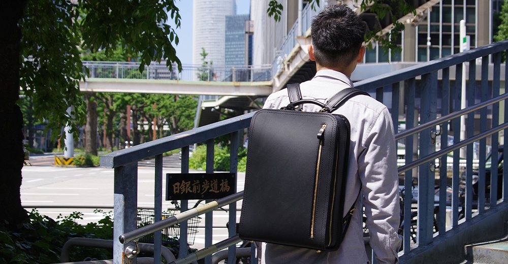 黑色皮革商務電腦後背包，側邊有金色拉鍊，適合日常通勤與商務使用。