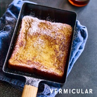 琺瑯鑄鐵玉子燒平底鍋，黑色鍋身搭配木質手柄，鍋內盛放著灑有糖粉的法式吐司，置於藍色布墊上。