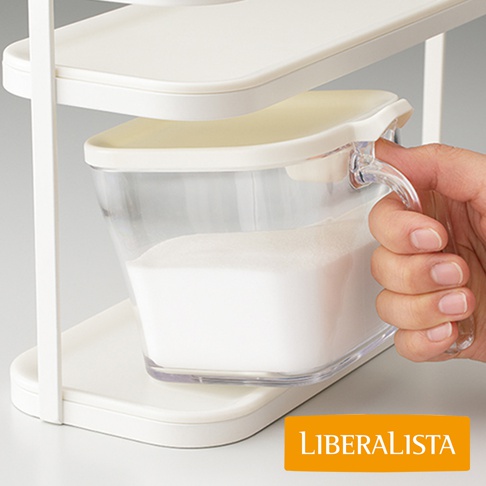LIBERALISTA 品牌白色收納架上，一個透明的罐子裝滿了白色粉末，一只手正要拿起罐子。