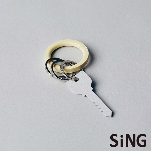 淺黃色圓形的 SiNG QQ 彈性鑰匙圈，搭配三個金屬鑰匙環與一把銀色金屬鑰匙，整體呈現簡約風格，放置於淺灰色背景上。