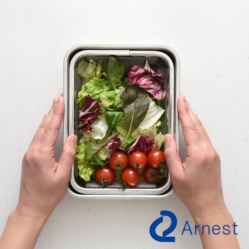 Arnest 不鏽鋼濾網保鮮盒內盛裝著新鮮的生菜沙拉與小番茄，雙手正扶著保鮮盒。