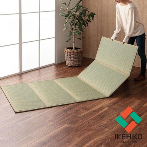 YUME 藺草組合式五折疊榻榻米睡墊，淺綠色，藺草編織材質，鋪設在木質地板上，部分折疊展開，一旁有盆栽植物和一位女士。