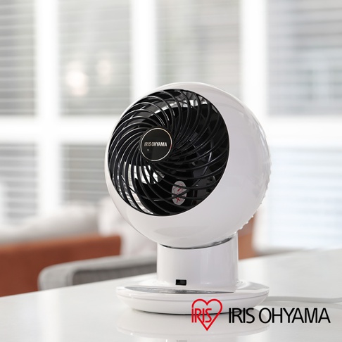 白色圓形空氣循環扇，黑色扇網，配有IRIS OHYAMA 標誌，放置於白色底座上，背景為模糊的室內裝潢。
