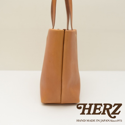 職人手作淺棕色皮革托特包，側面視角，展示簡約設計與天然皮革紋理。
