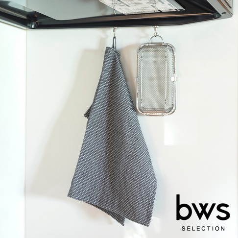 銀灰色網狀不鏽鋼洗碗機專用清潔收納盒，掛於牆上，旁邊掛著一條同色系的織紋抹布。