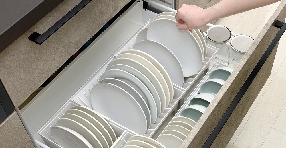 抽屜式餐盤收納架整齊擺放著許多白色盤子，架子旁還有幾個碗和玻璃罐。