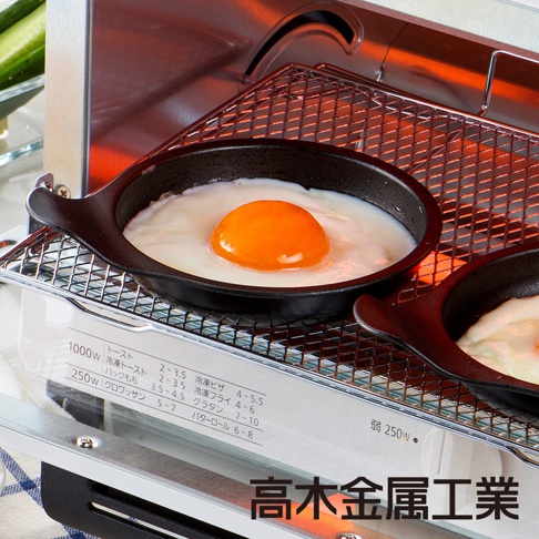 日本製烤箱用煎蛋圓形烤盤，黑色鑄鐵材質，內含一個煎蛋，蛋黃呈橘黃色，蛋白已凝固，烤盤放置於烤箱內網架上。