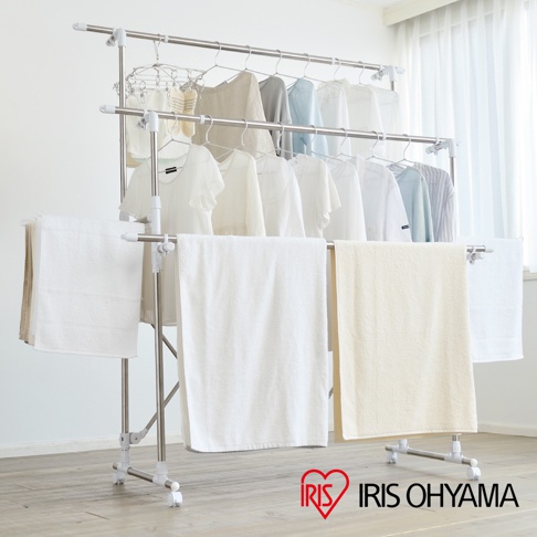 銀色金屬材質、多層設計的伸縮簡易組裝曬衣架，架上掛有數件白色、淺灰色、淺藍色及米色衣物，下方兩側垂掛白色毛巾，中間則掛著一條米色毛巾，整體結構穩固，附有輪子方便移動。