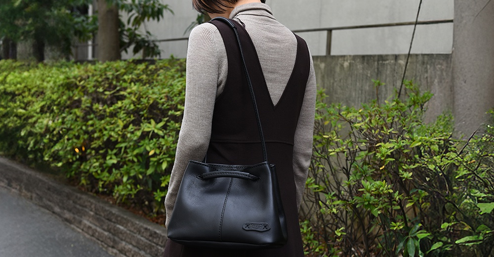 一個使用日本HERZ品牌Q-14皮革手提肩背包，配有可調式提把和束口設計，包身有縫線裝飾和一個方形logo標籤。