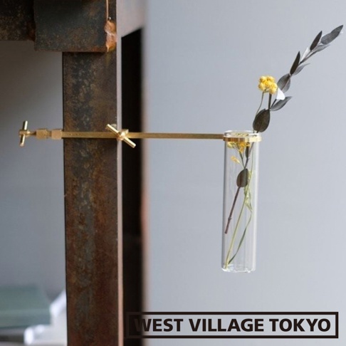 黃銅可夾式玻璃花器，帶有兩個黃銅夾子，固定在生鏽金屬架上，玻璃試管中插有乾燥植物，有黃色小花和深綠色葉子。